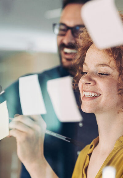 Een vrouw en een man schrijven op post-it briefjes die voor een raam hangen.