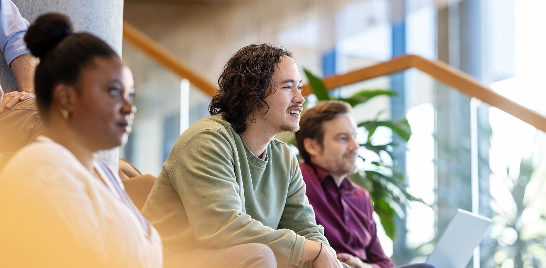 Focus op drie mensen in een collegezaal die naar een presentatie luisteren