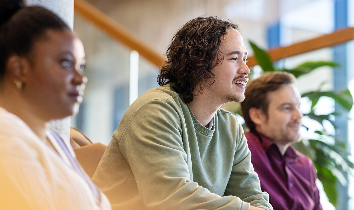 Focus op drie mensen in een collegezaal die naar een presentatie luisteren